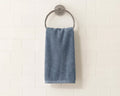 A blue-gray cotton hand towel hangs from a round silver metal towel ring mounted on a white subway tile wall.