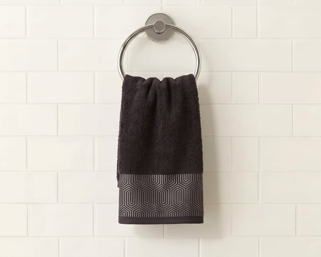 A dark charcoal gray hand towel with a textured geometric pattern at the bottom, hanging from a silver metal ring on a white subway tile wall.