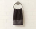 A dark charcoal gray hand towel with a textured geometric pattern at the bottom, hanging from a silver metal ring on a white subway tile wall.