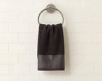 A dark charcoal gray hand towel with a textured geometric pattern at the bottom, hanging from a silver metal ring on a white subway tile wall.