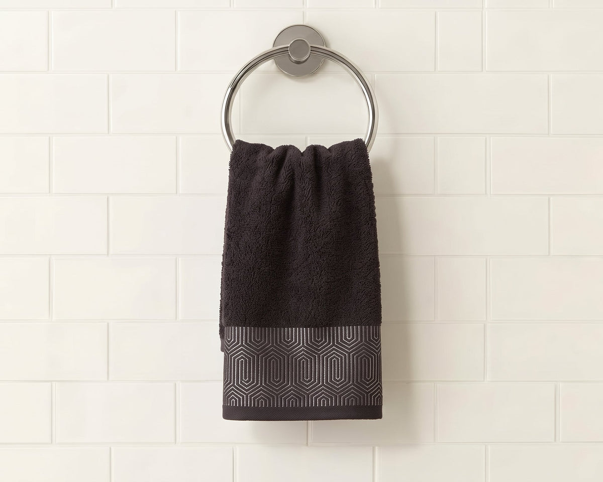 A dark charcoal gray hand towel with a textured geometric pattern at the bottom, hanging from a silver metal ring on a white subway tile wall.