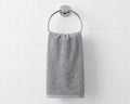 A gray cotton hand towel hanging from a silver metal ring on a white subway tile wall.