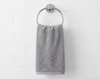 A gray cotton hand towel hanging from a silver metal ring on a white subway tile wall.