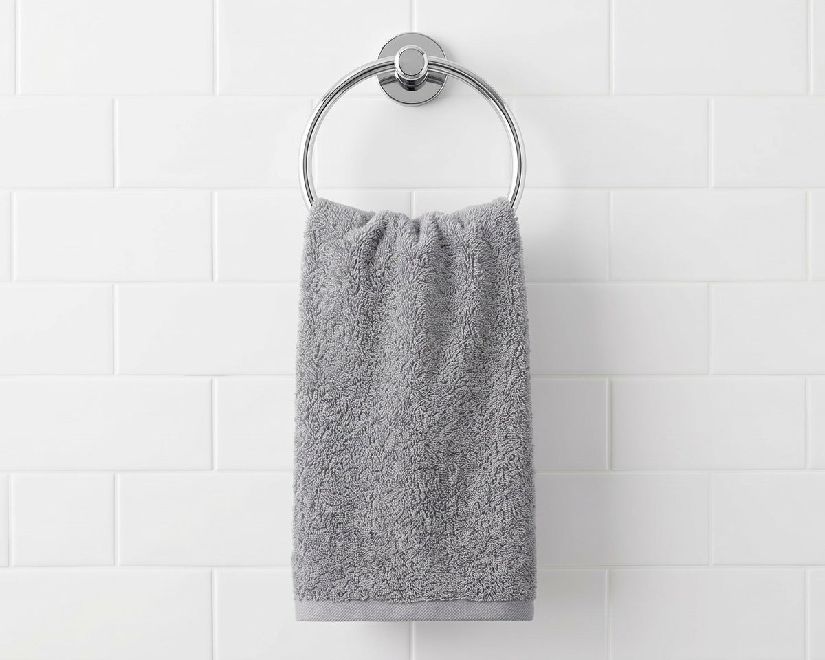 A gray cotton hand towel hanging from a silver metal ring on a white subway tile wall.