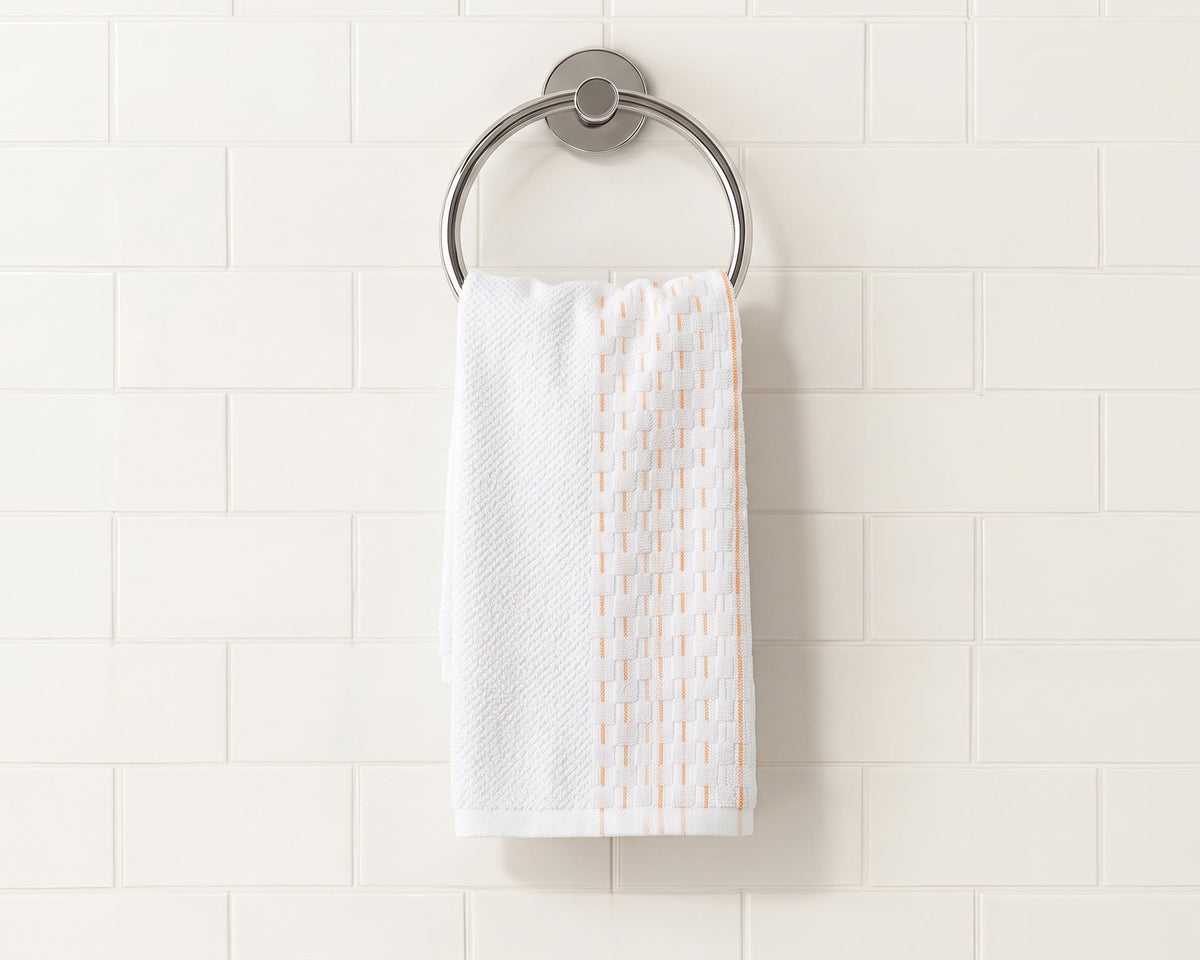 A white kitchen towel with a vertical peach-orange patterned stripe hangs from a round silver metal towel ring on a white subway tile wall.