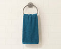 A teal blue towel hanging from a round silver metal ring on a white subway tile wall.