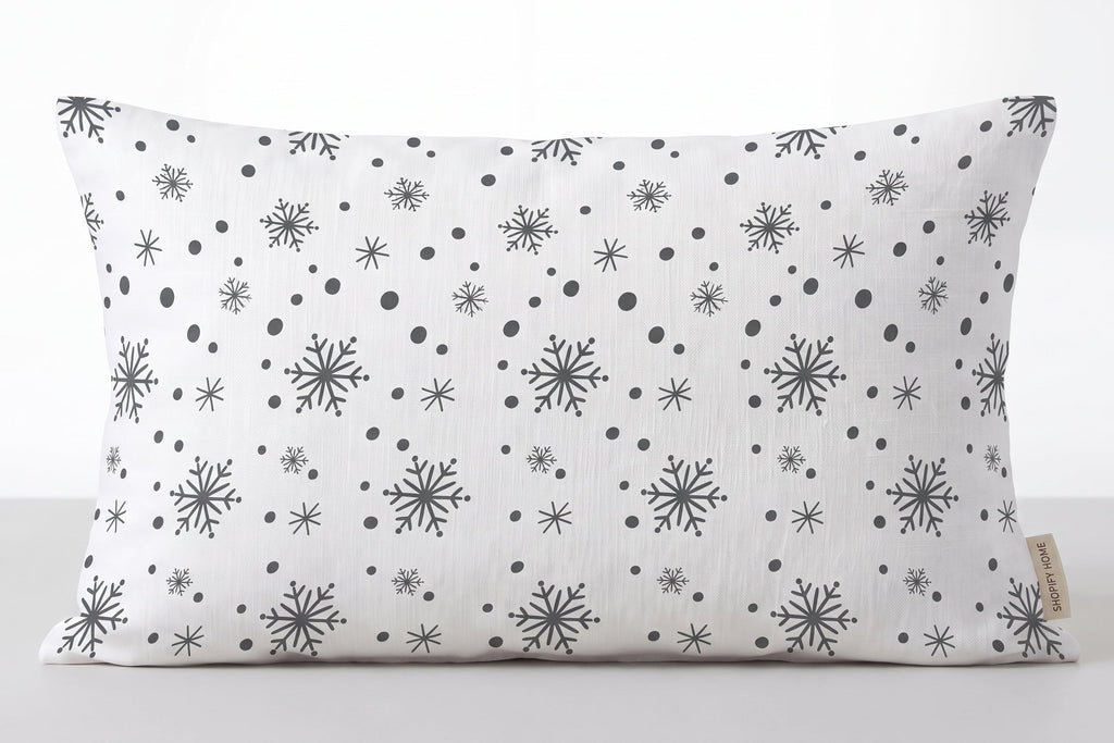 A rectangular lumbar pillow with a white background and a black snowflake and dot pattern, shown against a neutral light gray background.