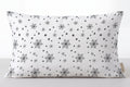 A rectangular lumbar pillow with a white background and a black snowflake and dot pattern, shown against a neutral light gray background.