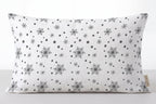 A rectangular lumbar pillow with a white background and a black snowflake and dot pattern, shown against a neutral light gray background.