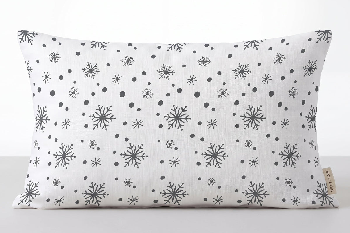 A rectangular lumbar pillow with a white background and a black snowflake and dot pattern, shown against a neutral light gray background.