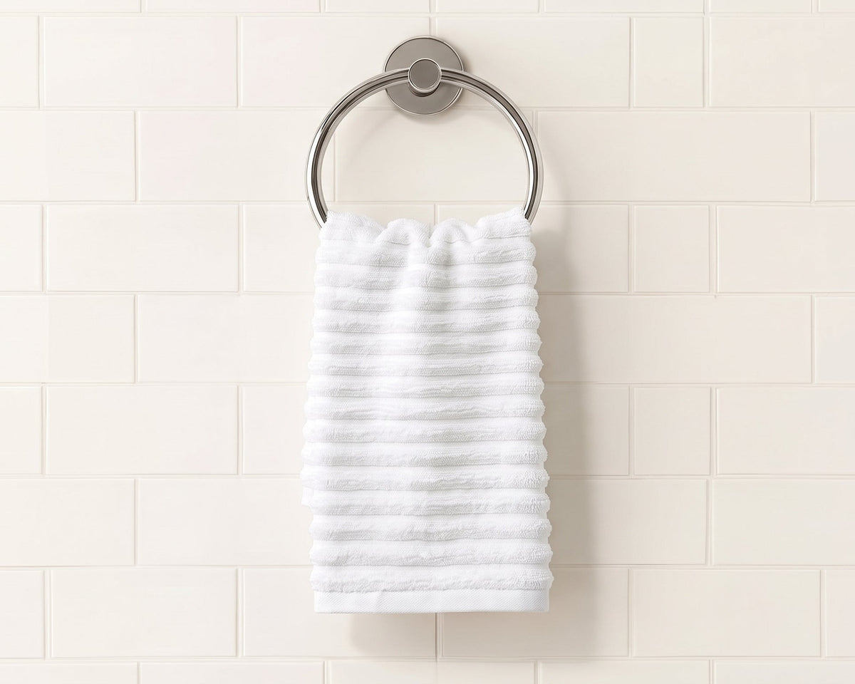 A white textured bath towel hanging from a round silver metal towel ring on a white subway tile wall.