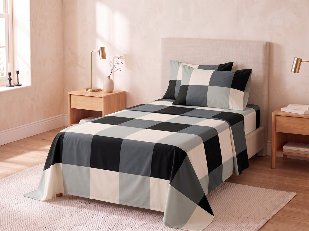 A bed dressed in a large buffalo check patterned comforter and matching pillow shams in black, gray, and cream, styled in a warm beige bedroom with wooden nightstands and lamps.