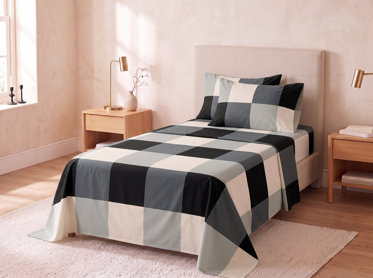A bed dressed in a large buffalo check patterned comforter and matching pillow shams in black, gray, and cream, styled in a warm beige bedroom with wooden nightstands and lamps.