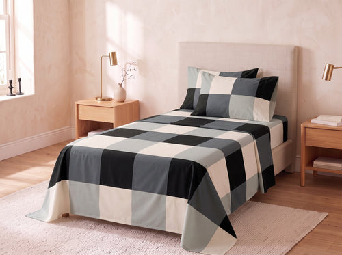 A bed dressed in a large buffalo check patterned comforter and matching pillow shams in black, gray, and cream, styled in a warm beige bedroom with wooden nightstands and lamps.
